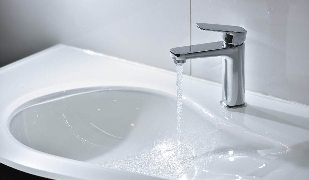 Chrome tap with open water that flows into a white sink