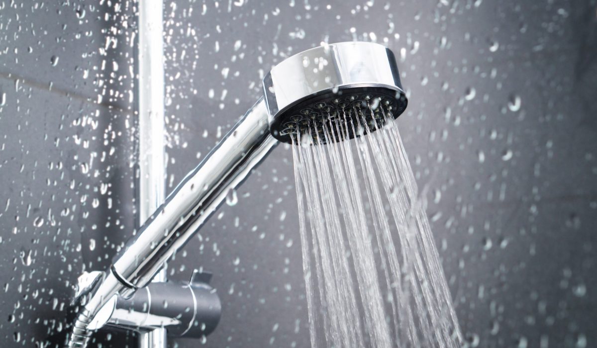 Fresh shower behind wet glass window with water drops splashing. Water running from shower head and faucet in modern bathroom.
